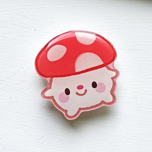 May include: A red and white mushroom with a smiling face and pink cheeks. The mushroom is made of resin and has a glossy finish.