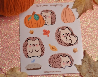 Puede incluir: Una hoja de pegatinas con adorables dibujos animados de erizos con temas otoñales. Las pegatinas incluyen erizos con calabazas, hojas y una tarta. El texto "Autumn Hedgehog" está en la parte superior de la hoja. El texto "Planet Bunnie" está en la parte inferior de la hoja.
