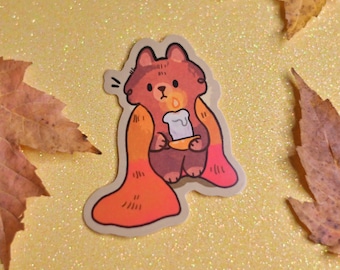 Puede incluir: Una pegatina con un mapache de dibujos animados que lleva una capa roja y naranja y sostiene una vela encendida. El mapache tiene una expresión de sorpresa en su rostro. La pegatina está sobre un fondo dorado brillante.