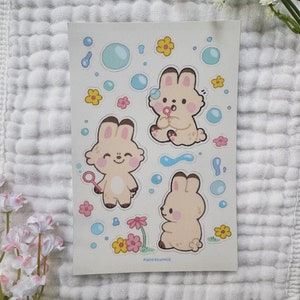 May include: A sheet of stickers featuring three cartoon bunnies blowing bubbles. The bunnies are light brown with pink cheeks and are surrounded by blue bubbles and yellow flowers. The text "planetbunnie" is at the bottom of the sheet.