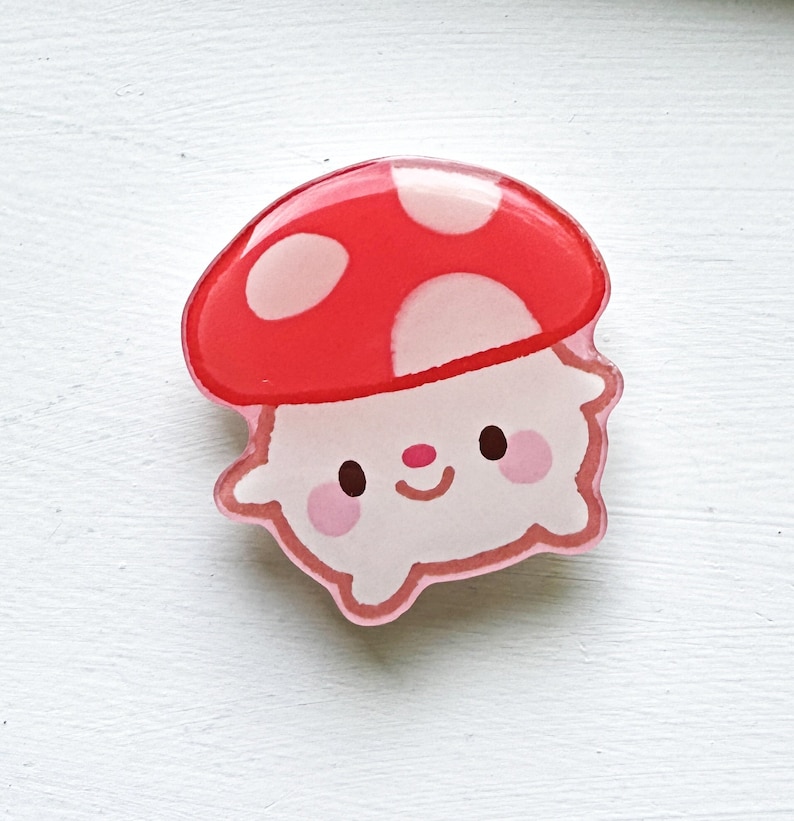 May include: A red and white mushroom with a smiling face and pink cheeks. The mushroom is made of resin and has a glossy finish.