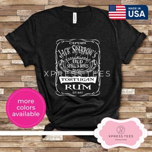 May include: Black t-shirt with a white graphic of a vintage rum label. The label reads "Captain Jack Sparrow's Old Skull 'n Bones Brand Tortuigan Rum Est. 1697".