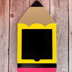May include: A pencil-shaped chalkboard featuring a black writing surface framed by a bright yellow body. The top section is tan with a black triangular tip, while the bottom section includes a black band above a pink eraser base.