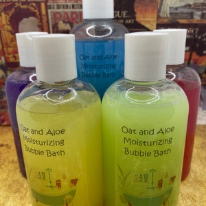 May include: Four bottles of bath products with white lids and labels that say "Oat and Aloe Moisturizing Bubble Bath". The bottles are filled with different colored liquids: blue, yellow, green, and red.