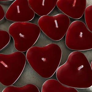 May include: A collection of heart-shaped red candles with white wicks, set in silver-colored metal holders. The candles are arranged closely together, creating a romantic and decorative display. Ideal for Valentine's Day or other special occasions.