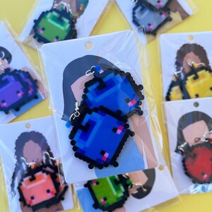 May include: Assortment of pixelated character earrings in various colors, including blue, green, red, yellow, and purple. The earrings are displayed on cards with illustrations of people wearing the earrings.