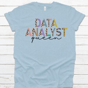 May include: Light blue t-shirt with the text "DATA ANALYST queen" in colorful letters with a leopard print pattern.