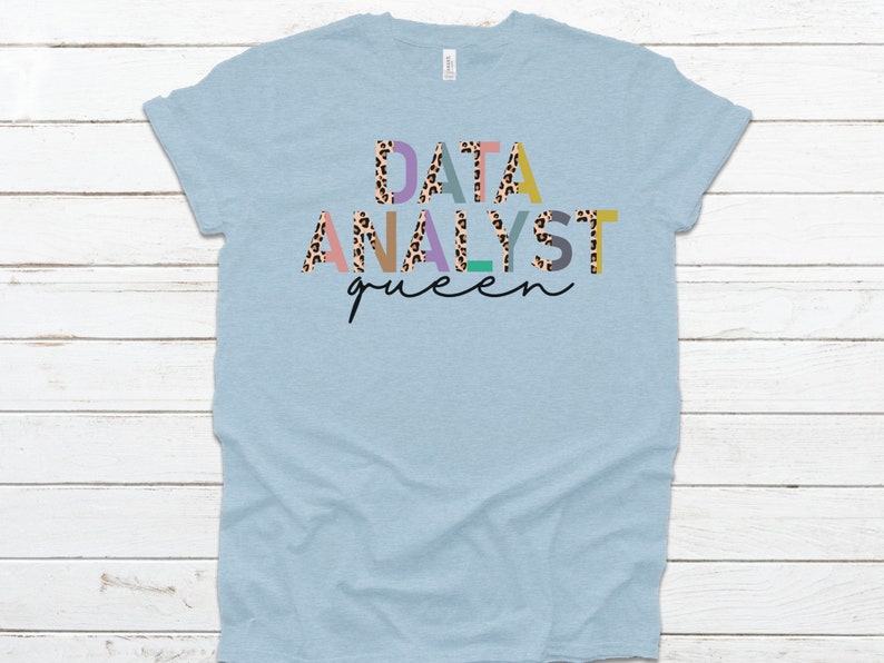 May include: Light blue t-shirt with the text "DATA ANALYST queen" in colorful letters with a leopard print pattern.