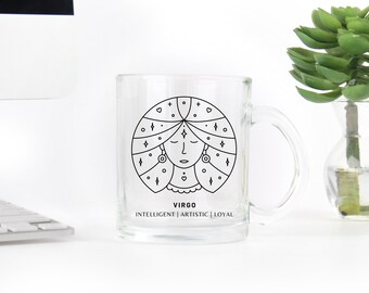 May include: A clear glass mug featuring a black line drawing of the Virgo zodiac sign. The design includes a stylized face within a circular frame, with the words "VIRGO" and the traits "INTELLIGENT | ARTISTIC | LOYAL" printed below.