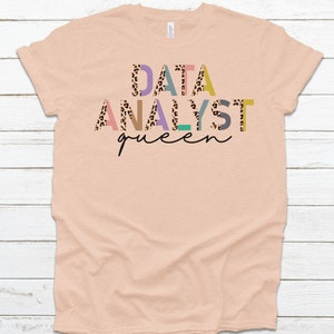 May include: A peach-colored t-shirt with the text "DATA ANALYST queen" in colorful letters with a leopard print pattern.