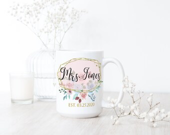 May include: White ceramic mug with a gold geometric frame and floral design. The text "Mrs. Jones EST. 03.25.2020" is printed on the mug.
