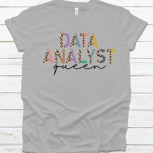 May include: Gray t-shirt with the text "DATA ANALYST queen" in colorful letters with a leopard print pattern.