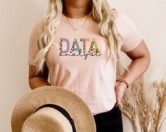 Könnte beinhalten: Ein pinkfarbenes T-Shirt mit dem Text "DATA analyst" in bunten Buchstaben mit Leopardenmuster.