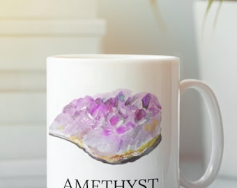 May include: White ceramic mug with a watercolor illustration of an amethyst crystal. The text "Amethyst" is printed below the crystal, along with the words "Protective | Calm | Peace".