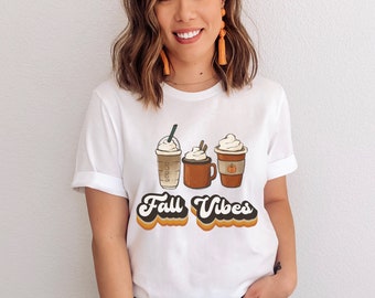 May include: White t-shirt with a graphic of three coffee drinks with whipped cream and the text "Fall Vibes" in a retro font.