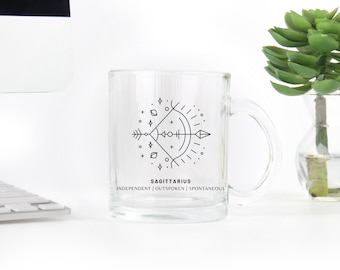 May include: A clear glass mug with a black and white graphic of the Sagittarius zodiac symbol and the text "SAGITTARIUS INDEPENDENT | OUTSPOKEN | SPONTANEOUS".
