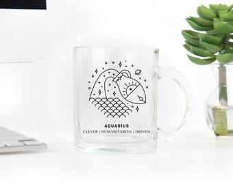 May include: A clear glass mug with a black line drawing of an Aquarius zodiac sign. The sign is a stylized image of a water pitcher with waves and stars. The text "Aquarius" is below the image, and the text "Clever | Humanitarian | Driven" is below that.