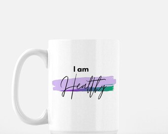 May include: White ceramic mug with a black and white design that says "I am Healthy" with a purple, blue, and green brushstroke behind the text.