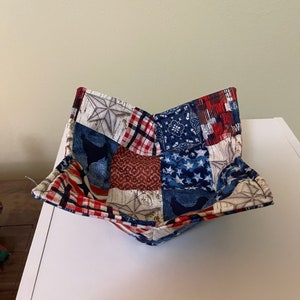 May include: A red, white, and blue patchwork fabric bowl. The bowl is made of squares of different fabrics with stars, stripes, and plaid patterns.