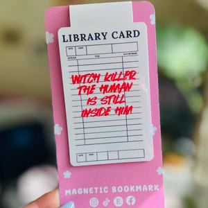 Könnte beinhalten: Ein pinkfarbener magnetischer Lesezeichen mit einem weißen Bibliothekskartendesign. Die Karte trägt den Text "WITCH KILLER THE HUMAN IS STILL INSIDE HIM" in Rot. Auf dem unteren Teil des Lesezeichens steht "MAGNETIC BOOKMARK" und die Social-Media-Konten des Verkäufers.