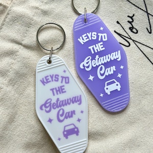 May include: Two purple and white keychains shaped like motel keys. The keychains have the text "Keys to the Getaway Car" with a small car icon.