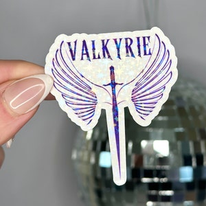 May include: A white sticker with a holographic finish featuring a sword with wings and the word "VALKYRIE" in purple lettering.
