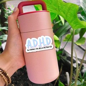 May include: A pink reusable water bottle with a red handle and a sticker that says "A.D.H.D. Aw Damn, I'm hella distracted."