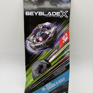 K&ouml;nnte beinhalten: Eine verpackte Beyblade X Spielzeug-Set. Die Verpackung ist schwarz mit dem Beyblade X Logo und japanischem Text. Das Spielzeug ist durch ein transparentes Fenster sichtbar. Der Text "Keel Shark 3-60LF" ist auf der Verpackung aufgedruckt, zusammen mit "Let it Rip!"