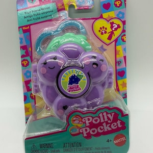 May include: A purple grape-shaped Polly Pocket Fruit Friend Reveal toy in its original packaging. The plastic case features a smiling face, a green stem handle, and a central circular sticker with a grape graphic and the Polly Pocket logo.
