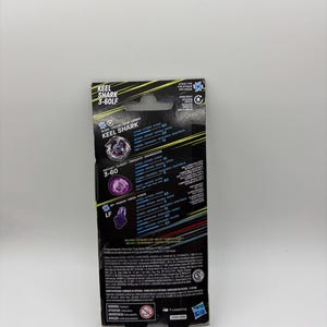 K&ouml;nnte beinhalten: Eine schwarz-gelbe Box f&uuml;r ein Keel Shark 3-60LF Spielzeug. Die Box zeigt den Namen des Spielzeugs, eine Grafik des Spielzeugs und verschiedene Leistungsstatistiken. Die Box hat ein Aufh&auml;ngeloch und das Hasbro-Logo.