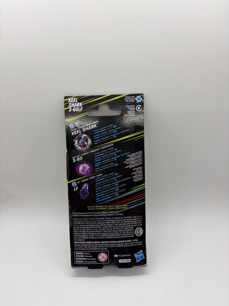 K&ouml;nnte beinhalten: Eine schwarz-gelbe Box f&uuml;r ein Keel Shark 3-60LF Spielzeug. Die Box zeigt den Namen des Spielzeugs, eine Grafik des Spielzeugs und verschiedene Leistungsstatistiken. Die Box hat ein Aufh&auml;ngeloch und das Hasbro-Logo.