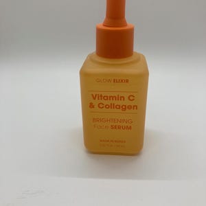 Puede incluir: Botella de sérum facial teñida de naranja con cuentagotas. La etiqueta dice "GLOW ELIXIR Vitamin C & Collagen Brightening Face Serum". La botella contiene 50 ml de sérum. Fabricado en Corea.