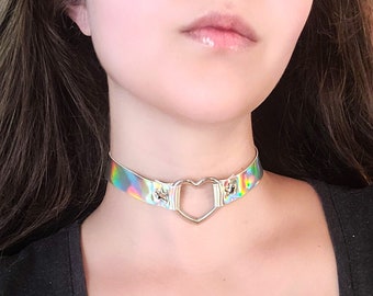 Op de afbeelding: Een zilveren hartvormige choker met een holografische regenboogkleurige band.