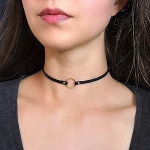 Pode incluir: Um colar choker de couro preto com um pingente circular dourado.