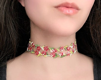 May include: A delicate floral choker necklace with pink and green embroidered flowers on a sheer fabric base.