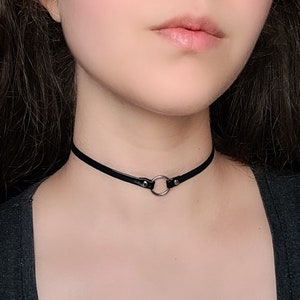 May include: A black leather choker necklace with a silver ring accent.