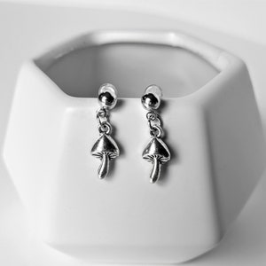 May include: A pair of silver mushroom dangle earrings. The earrings have a small silver ball at the top and a silver mushroom charm hanging from it.