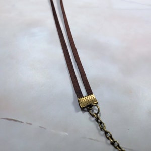 May include: A brown leather cord necklace with a gold-toned clasp. The cord is double-layered and the clasp has a textured design.
