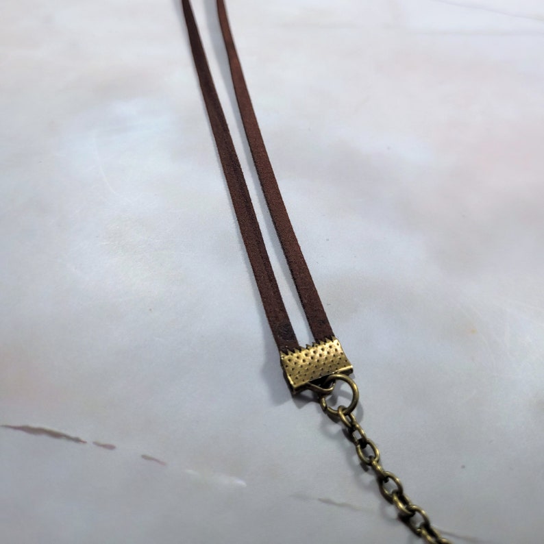 May include: A brown leather cord necklace with a gold-toned clasp. The cord is double-layered and the clasp has a textured design.