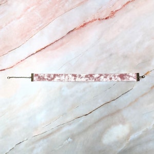 Op de afbeelding: Een roze fluwelen choker met een zilveren ketting en metalen sluitingen.