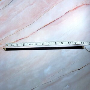 Puede incluir: Un collar gargantilla negro, de aproximadamente 30 cm de largo, con un cierre y una cadena de color plateado. El collar est&aacute; hecho de un material fino y aterciopelado. El fondo es un patr&oacute;n de m&aacute;rmol rosa claro y blanco.