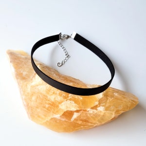May include: A black leather choker necklace with a silver chain closure. The necklace is lying on a piece of yellow rock.