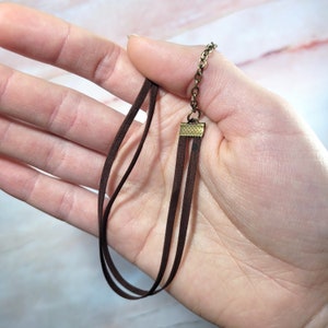 May include: A brown suede cord necklace with a gold-toned clasp. The necklace is layered with three strands of cord.