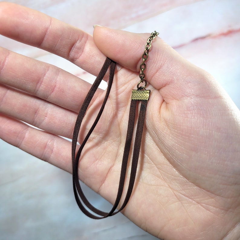 May include: A brown suede cord necklace with a gold-toned clasp. The necklace is layered with three strands of cord.