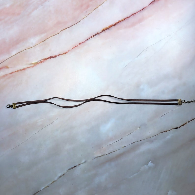 May include: A brown leather choker necklace with two strands and gold-toned metal clasps.