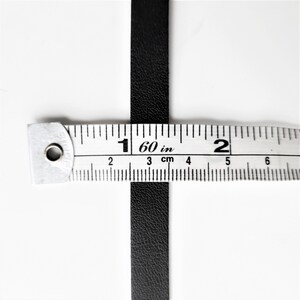 May include: A black leather strip measured with a ruler. The ruler shows 1 60/in and 2 inches.