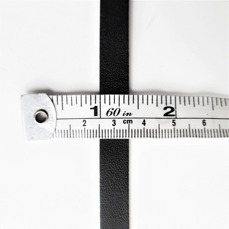 May include: A black leather strip measured with a ruler. The ruler shows 1 60/in and 2 inches.