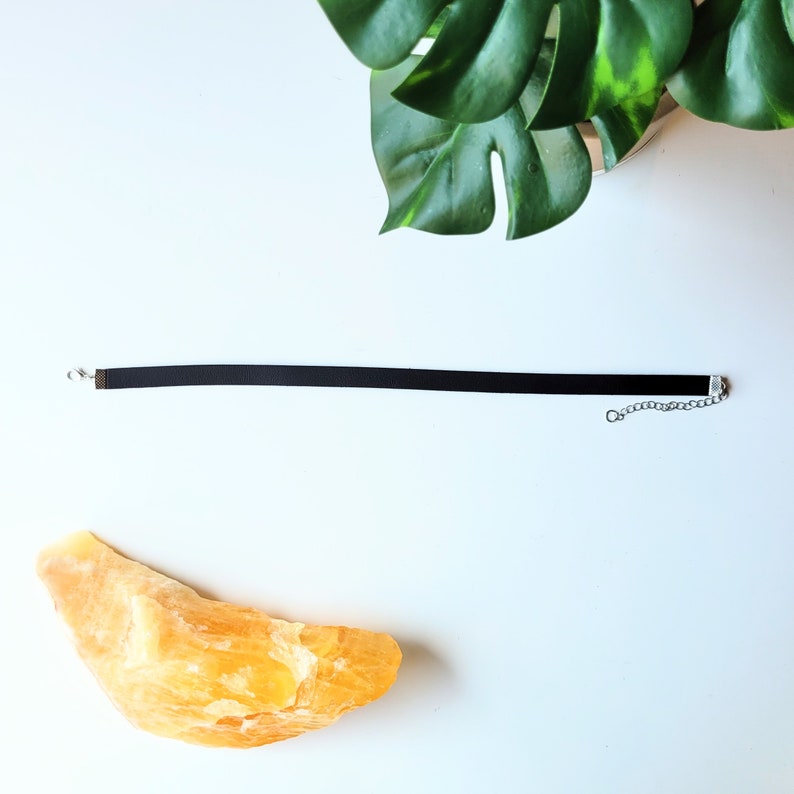 May include: A black choker necklace with a silver chain and clasp. The necklace is laying flat on a white surface.