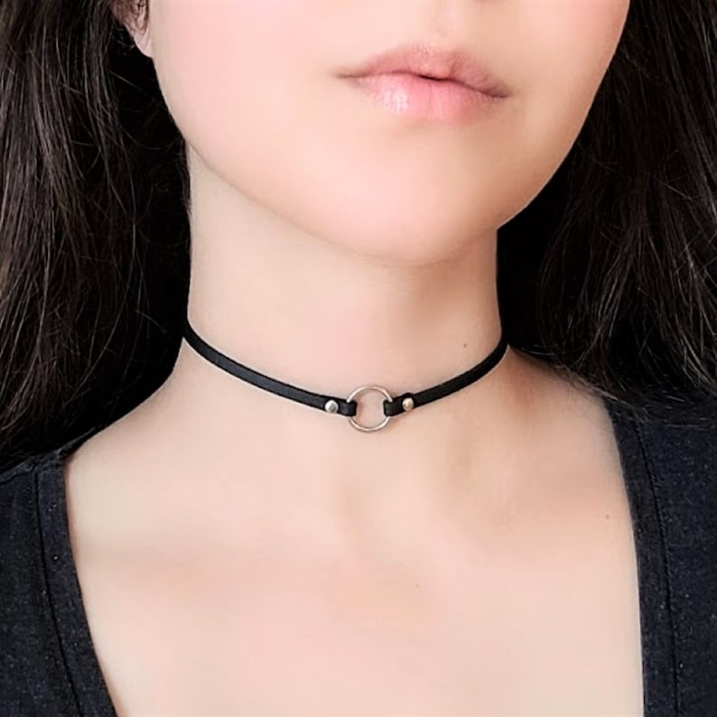 May include: A black leather choker necklace with a silver circle pendant.