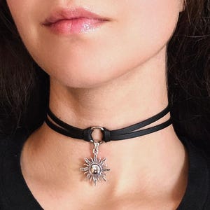 May include: A black leather choker necklace with a silver sun pendant. The choker is adjustable and has a simple design.